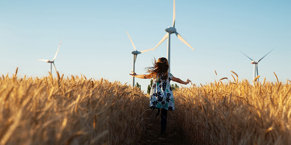 Een meisje in een bloeiend veld met windmolens op de achtergrond, vrolijk de natuur bewonderend.