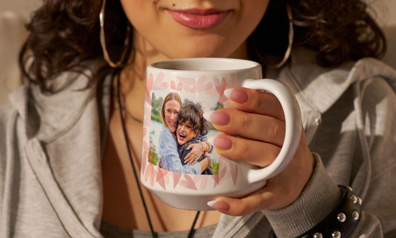 Iemand houdt een gepersonaliseerde koffiemok met een foto van twee lachende mensen vast.
