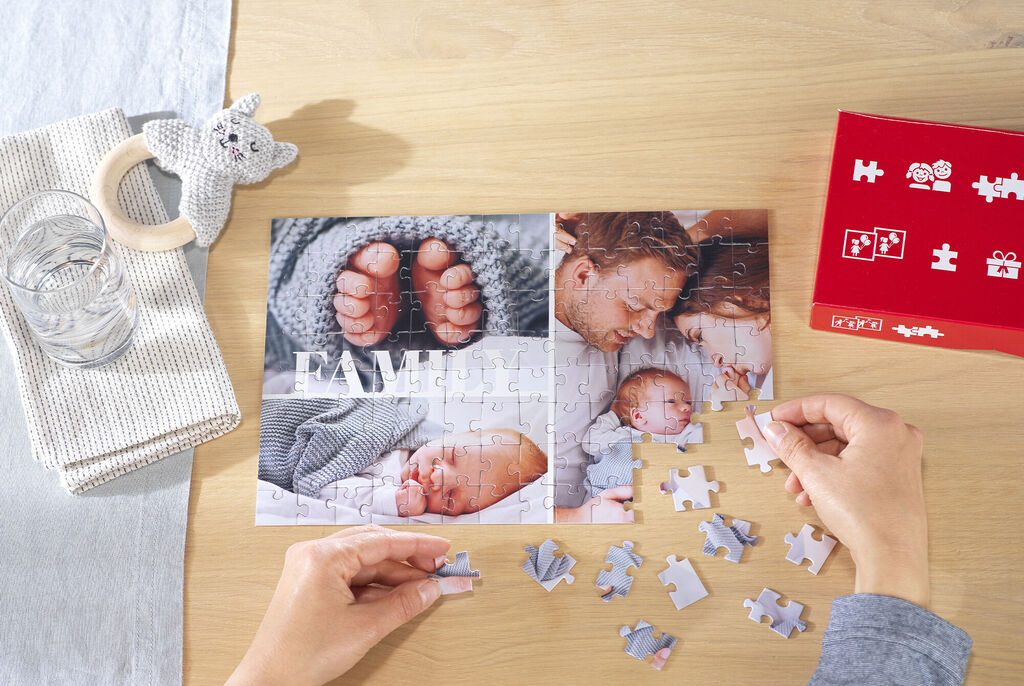 Handen leggen een gepersonaliseerde fotopuzzel met babyfoto’s aan een houten tafel, naast de bijbehorende puzzeldoosHanden leggen een gepers