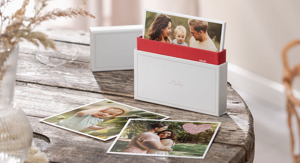 CEWE art prints in een witte doos op een houten tafel, omringd door nog meer art prints.